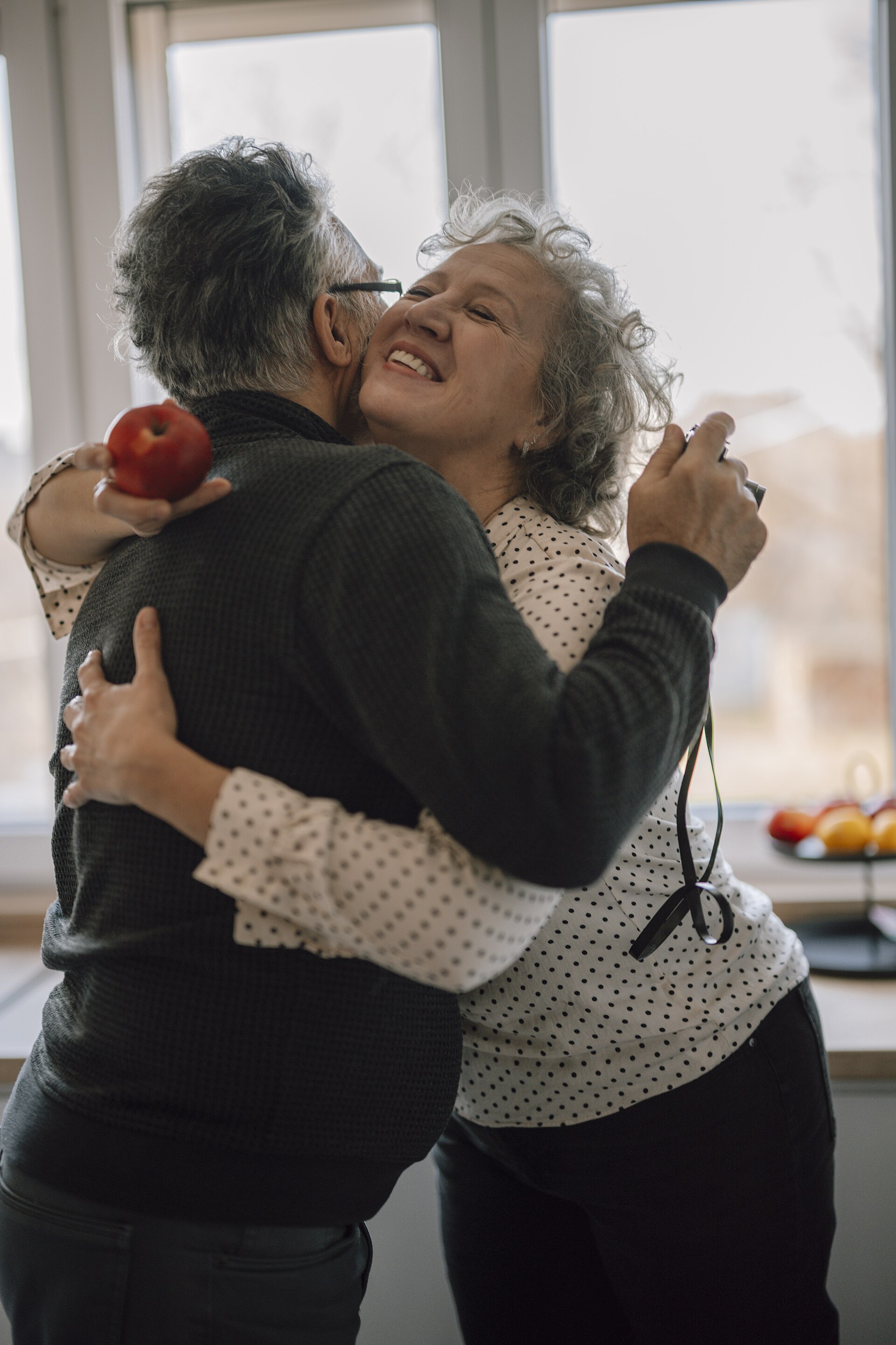 A smiling older woman hugging her husband in a bright kitchen
